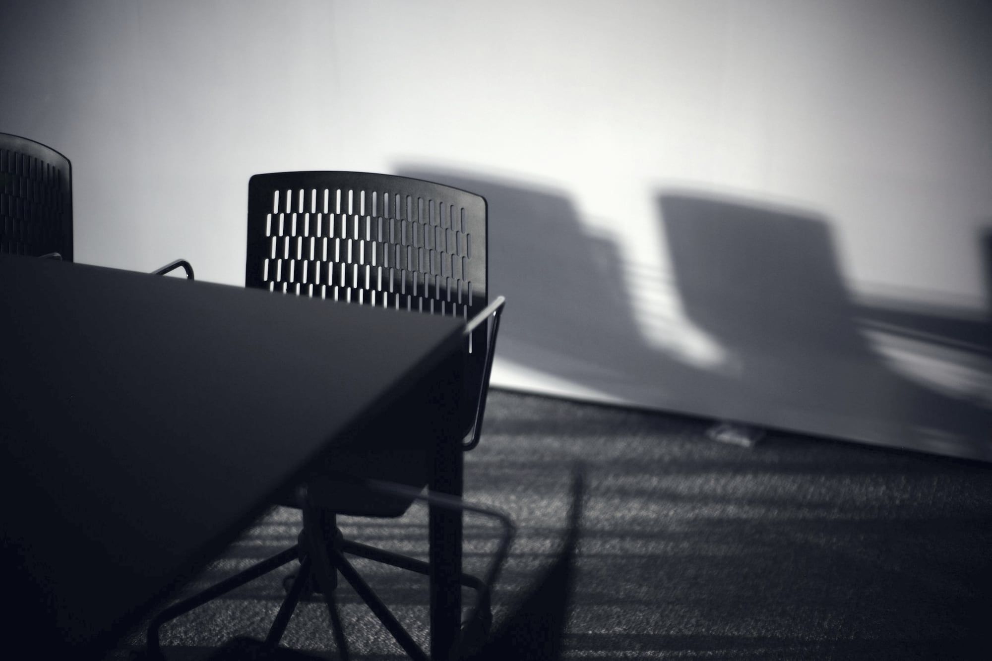 The edge of an empty meeting table and a chair, with window light and long shadows on the wall.