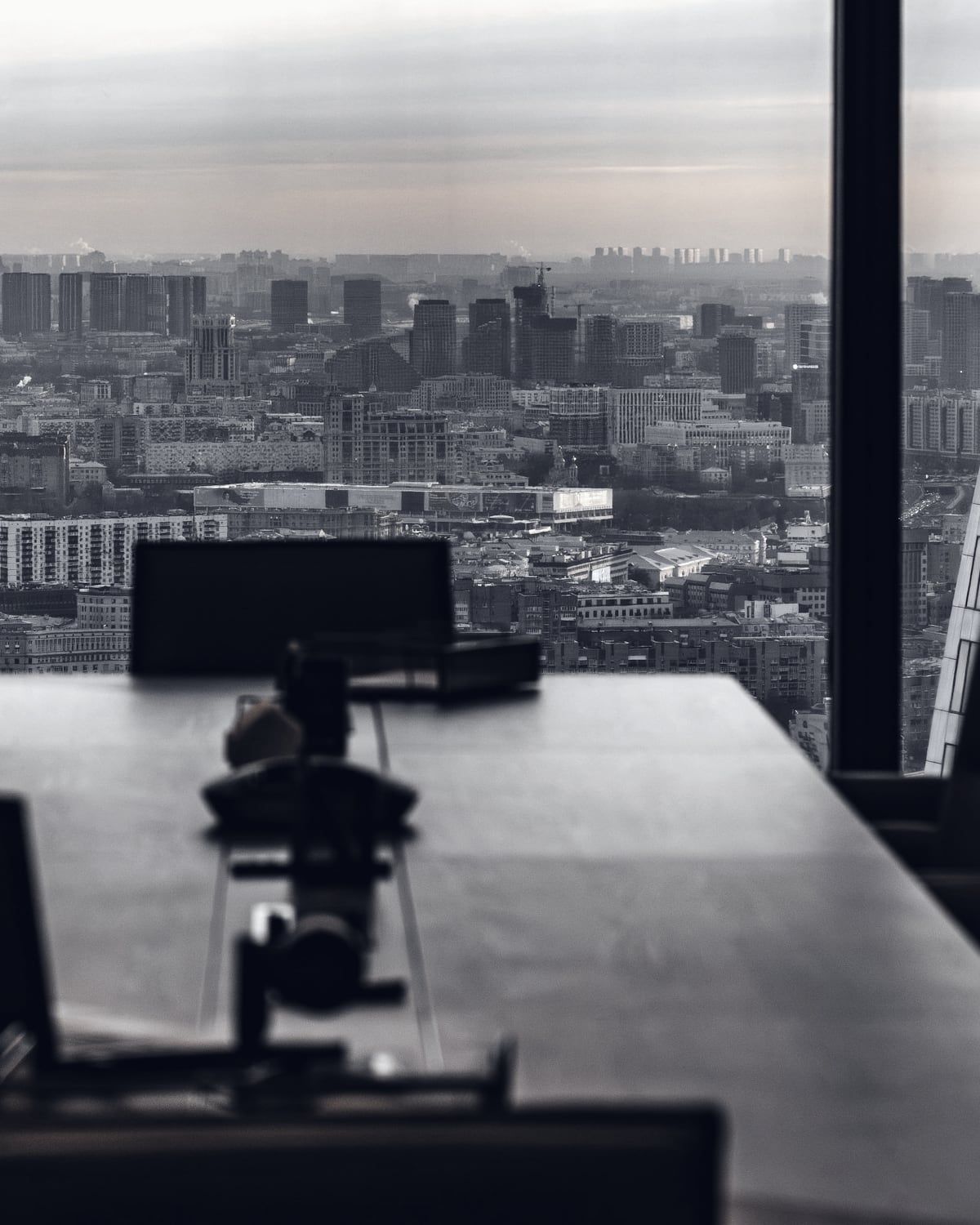 An empty boardroom table facing floor-to-ceiling windows over a city.